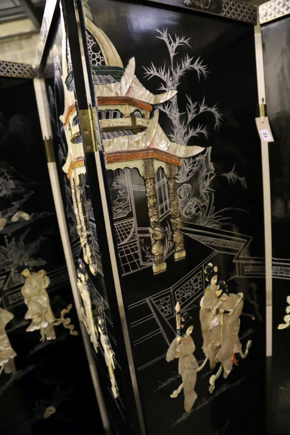 A Japanese black-lacquered and painted four-fold screen with applied decoration of geishas and temple, each panel 46 x 182cm